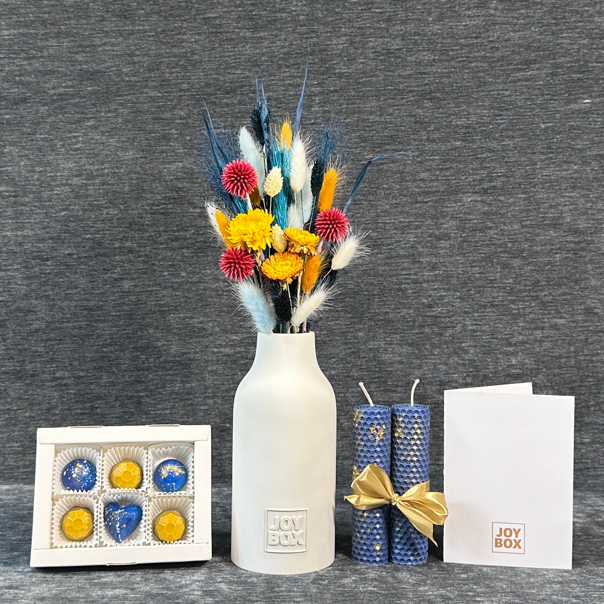 Подарунковий набір «Аквамаринова магія» JOY BOX: букет сухоцвітів у білій гіпсовій вазі, сині вощинні свічки, коробка синьо-золотих цукерок і біла листівка на сірому фоні