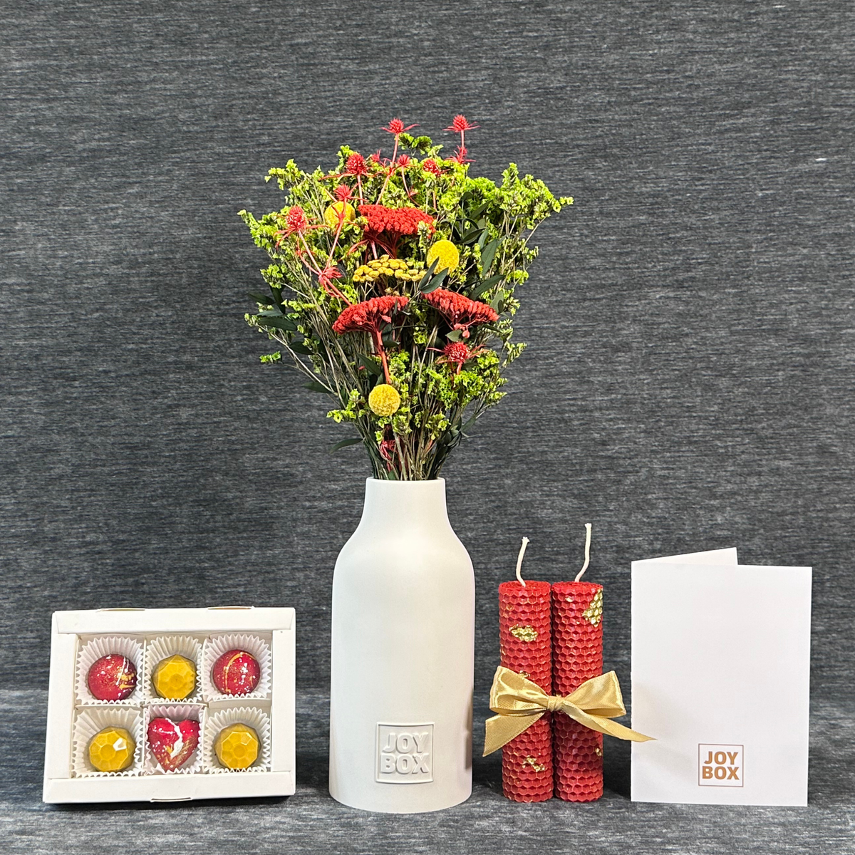 Подарунковий набір «Лаймовий дощ» JOY BOX: букет сухоцвітів у білій гіпсовій вазі, сині вощинні свічки, коробка синьо-золотих цукерок і біла листівка на сірому фоні