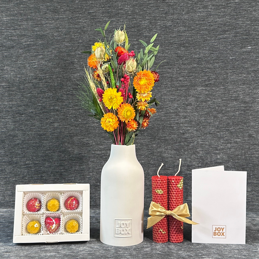 Подарунковий набір «Мандаринові чари» JOY BOX: букет сухоцвітів у білій гіпсовій вазі, сині вощинні свічки, коробка синьо-золотих цукерок і біла листівка на сірому фоні