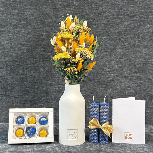 Подарунковий набір «Сонячний ранок» JOY BOX: букет сухоцвітів у білій гіпсовій вазі, сині вощинні свічки, коробка синьо-золотих цукерок і біла листівка на сірому фоні